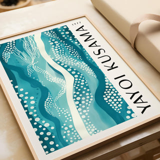 Framed close-up of abstract picture with teal waves and white dots on a table with beige wrapping
