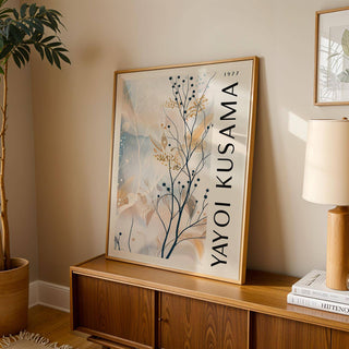 Large neutral wall art featuring delicate branches with berries leaning on a wooden console beside a lamp and plant