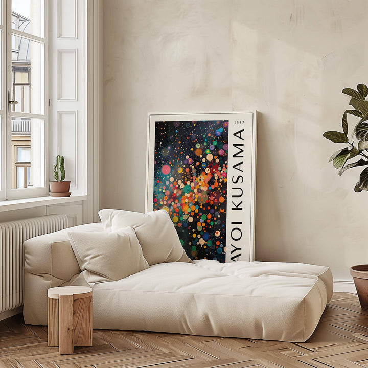 Print leaning on floor with colourful dots and black background beside plant and beige sofa