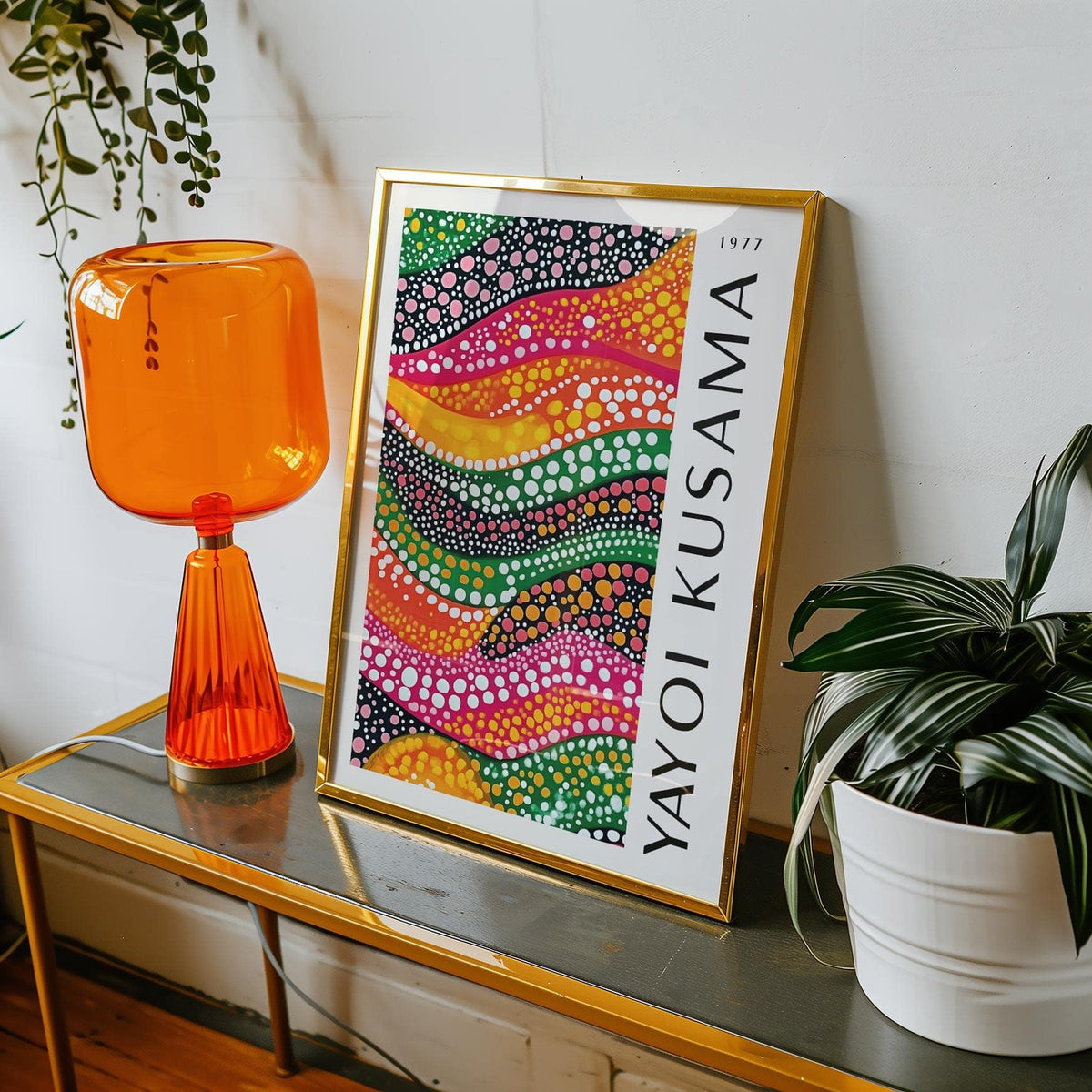 Framed print of polka dot art with colorful dotted waves beside an orange lamp and a green plant