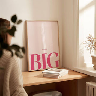 Print leaning on a desk with think big typography in pink and white and books nearby