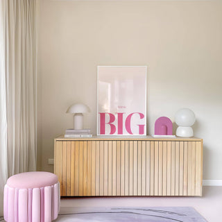 Print on a sideboard with pink typography and pale background with lamps and books