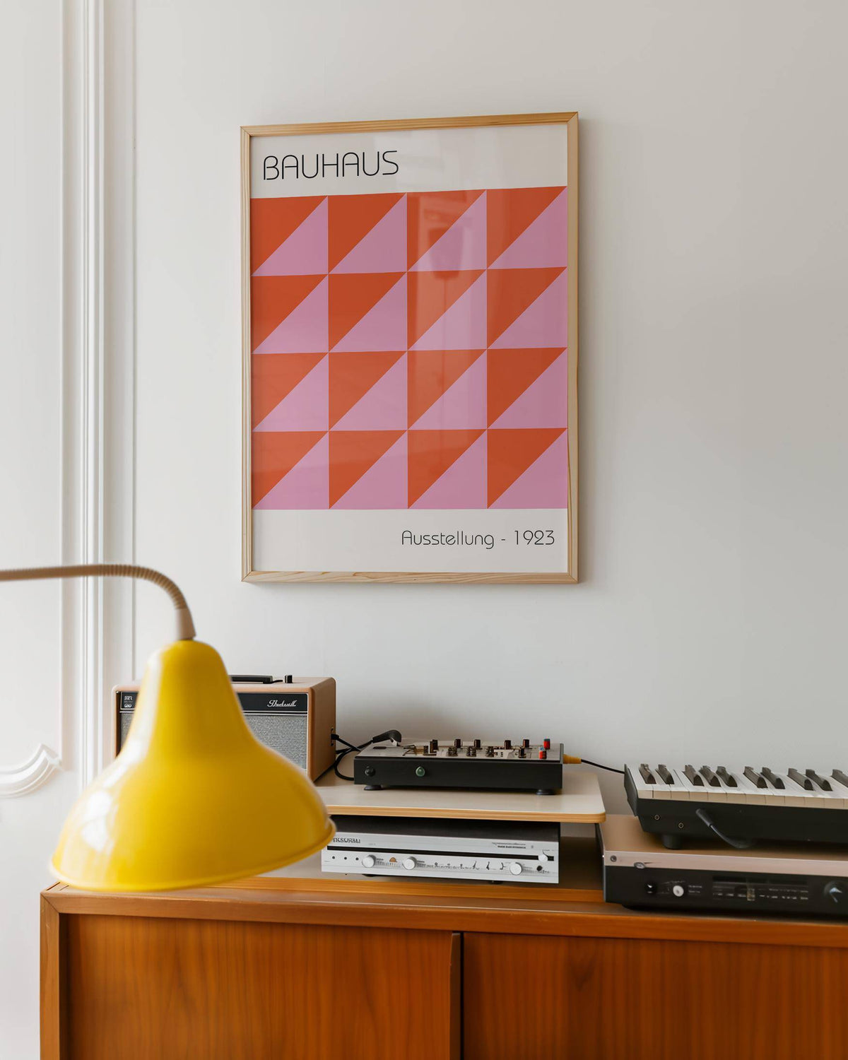 Modern wall art of red and pink geometric triangles framed above audio equipment and keyboard