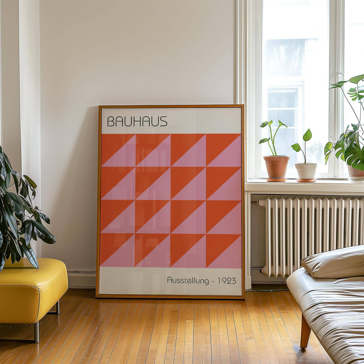 Print of modern wall art with red and pink geometric triangles leaning on a wooden floor near plants