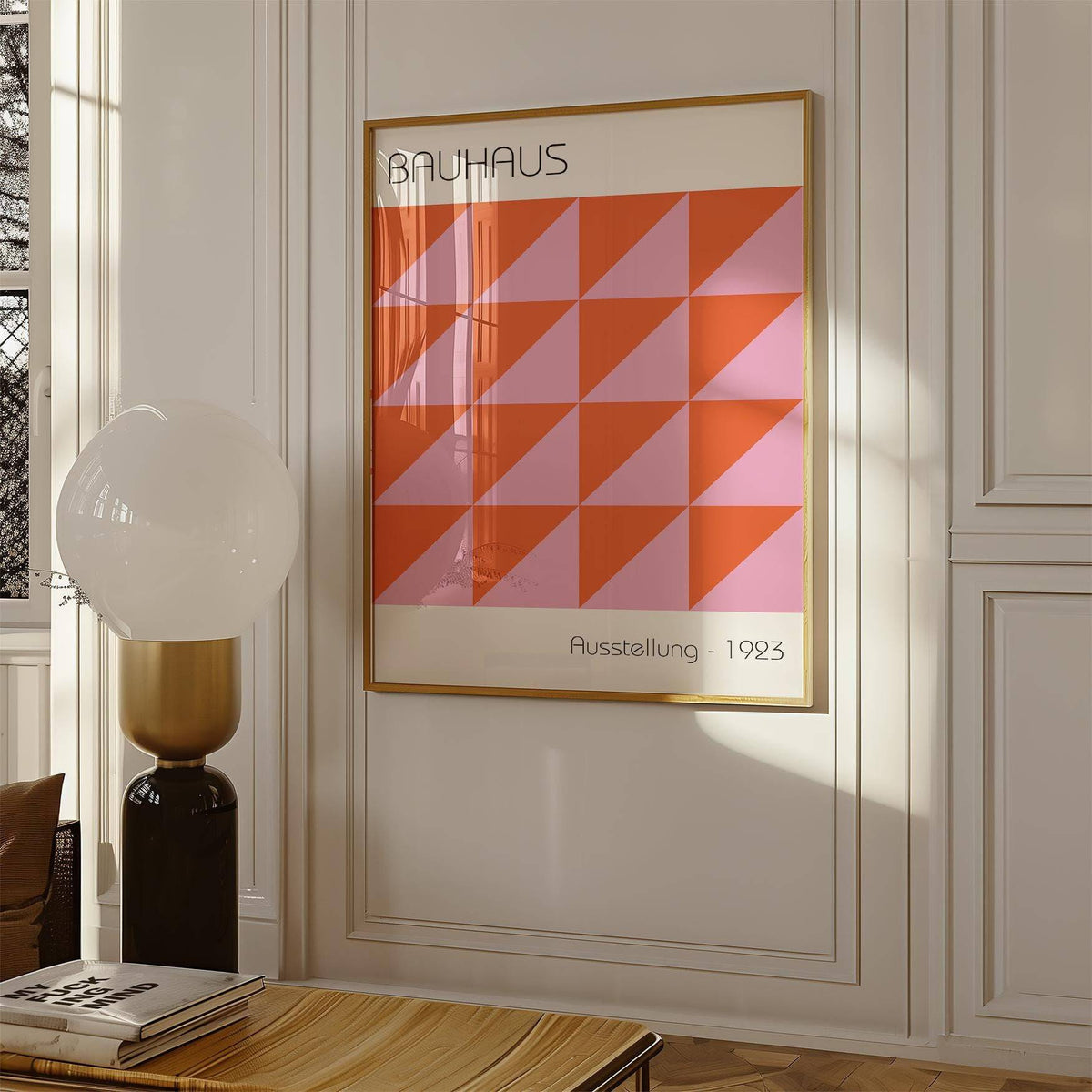 Modern wall art of red and pink geometric triangles framed on a white wall with a lamp nearby