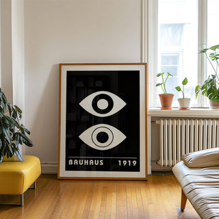 Eye Art print with abstract white eyes on black leaning by a window with plants in a living room