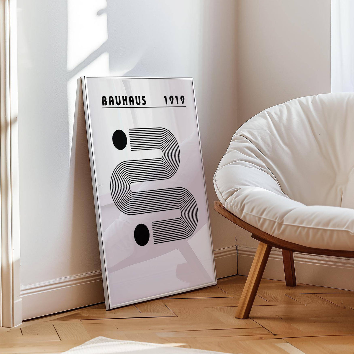 Black and White Minimalist Art print leaning on a floor by a white cushioned chair and wooden floor
