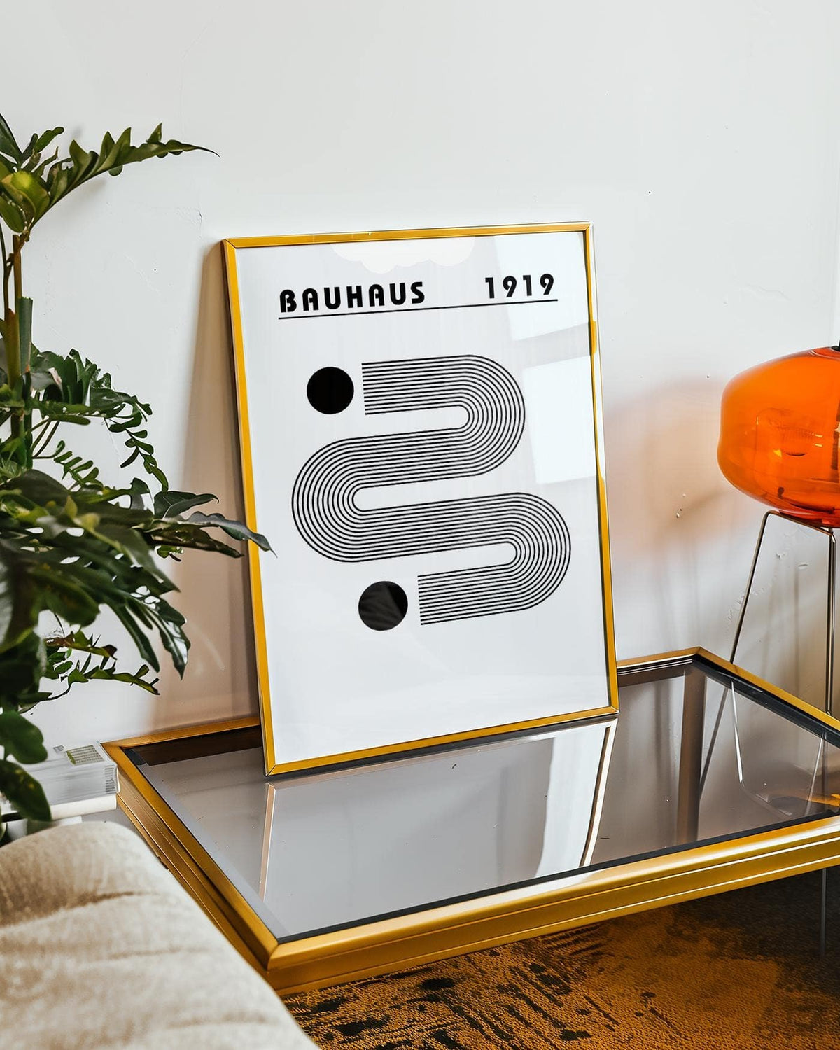 Black and White Minimalist Art print with gold frame leaning on a glass coffee table beside a green plant