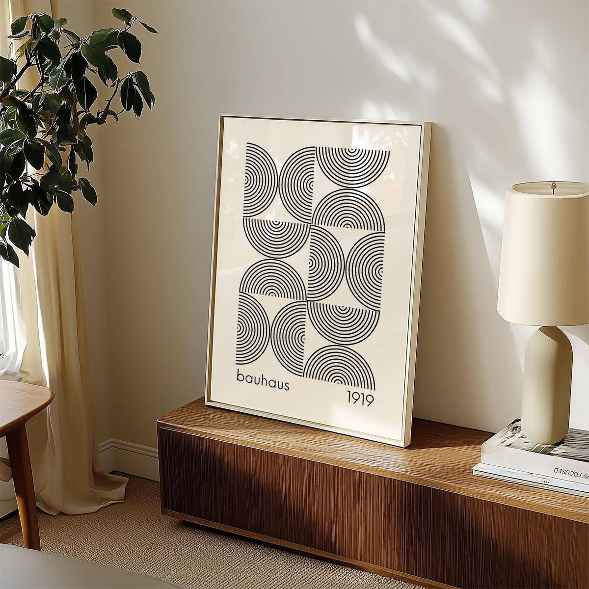 Framed Bauhaus wall art with black concentric semicircles on a wooden sideboard next to a lamp