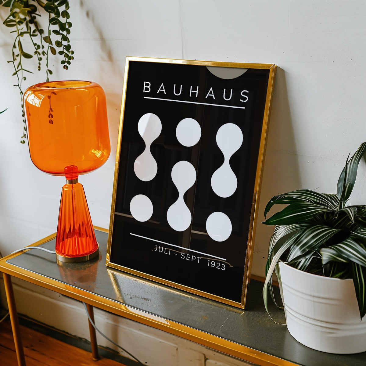 Framed Black and White Geometric Art print with Bauhaus text leaning on a glass table near orange lamp and plant