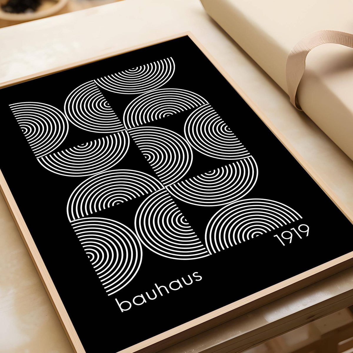 Framed Geometric wall art with white concentric circles on a black background placed on a wooden surface near a wrapped parcel