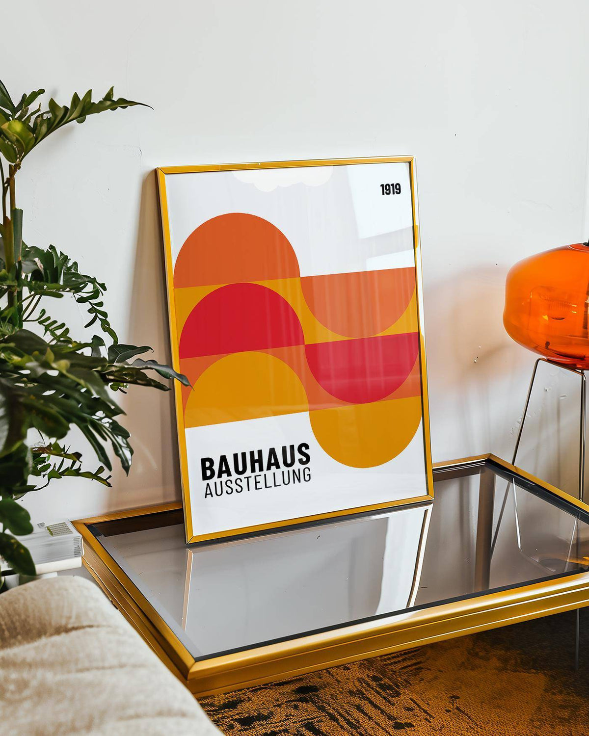 Print leaning on a glass coffee table with abstract geometric shapes in reds and orange beside a green plant