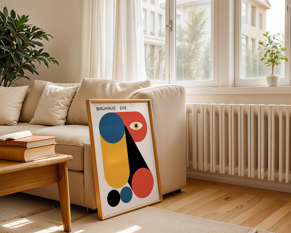 Print leaning on a floor beside a sofa featuring bauhaus graphic with geometric shapes in blue orange and black