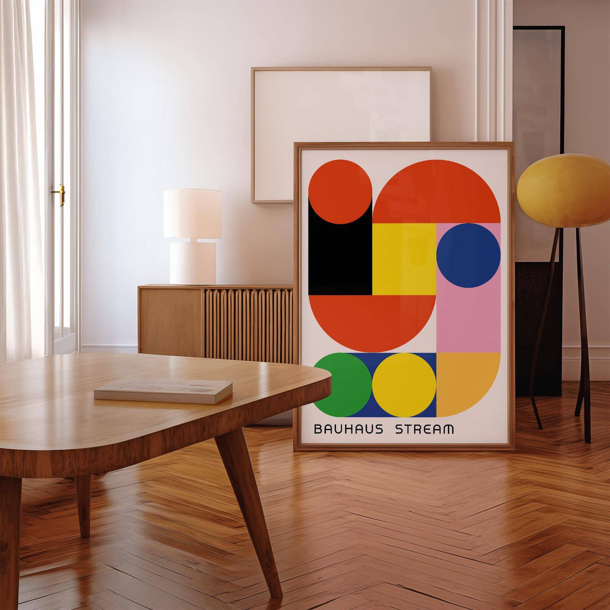 Print leaning on floor of geometric wall decal with colourful bauhaus shapes in a wooden frame near a lamp