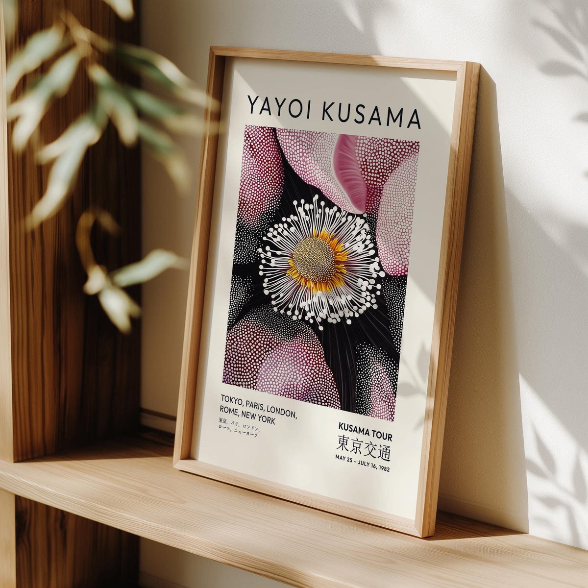 Print leaning on a shelf of an abstract flower bloom with pink and yellow tones near a plant