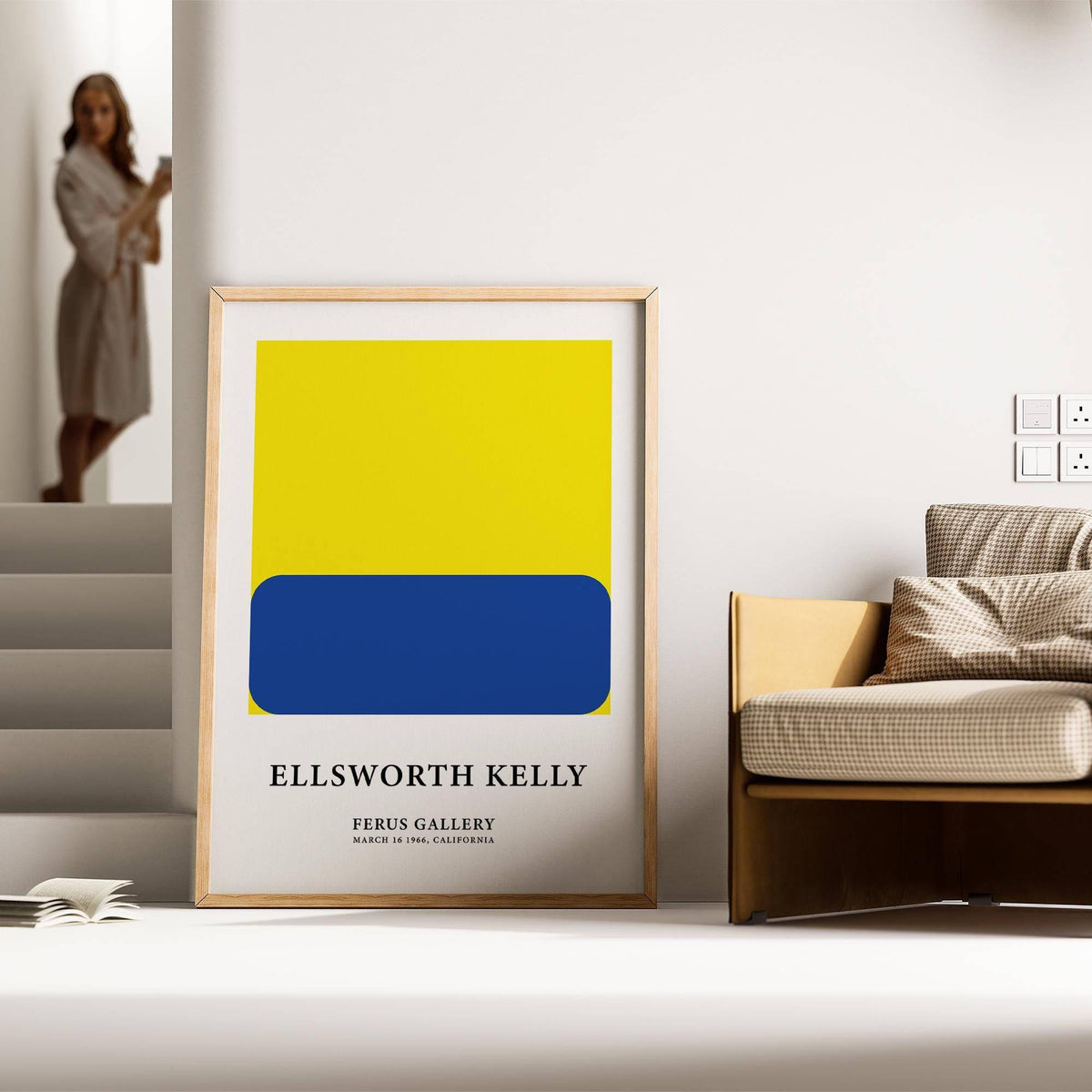 Minimalist artwork framed print with blue rounded rectangle on yellow square leaning against wall beside a sofa