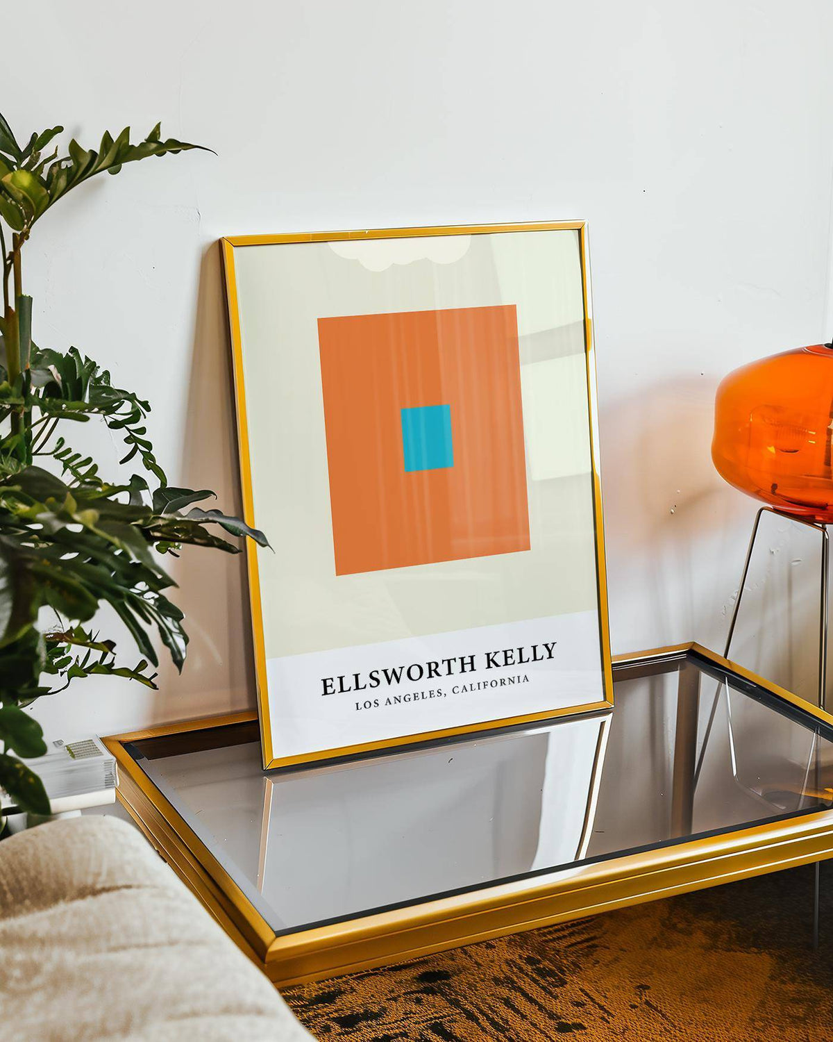 Ellsworth Kelly artwork leaning on glass table with gold frame and plant nearby