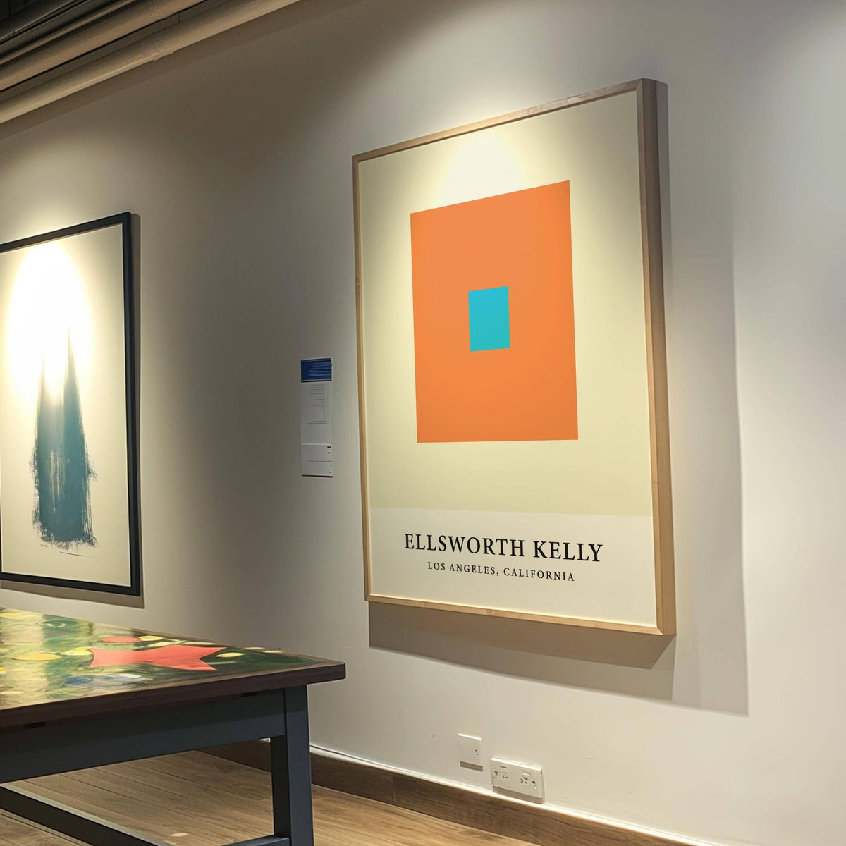 Ellsworth Kelly Artwork print with orange and blue squares in a gallery with a table nearby
