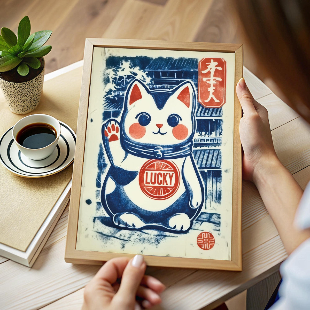 Framed Lucky Cat Charm print held in hands with a wooden table and cup nearby
