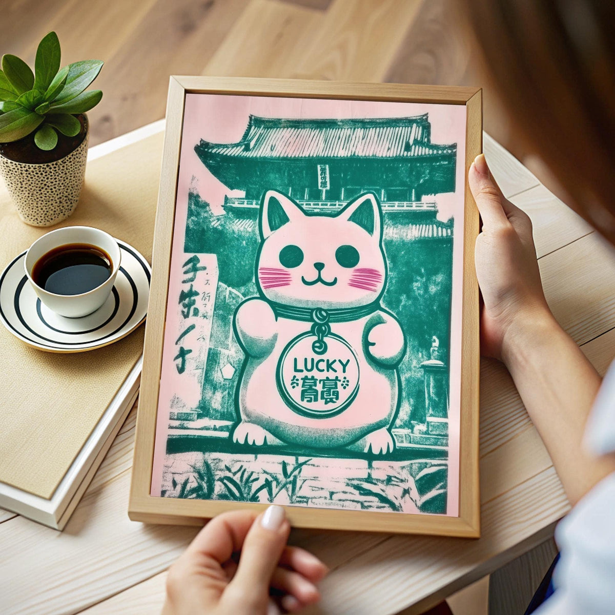 Framed print of a maneki-neko cat illustration with green and pink tones held in hands