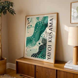 Black White and Green Poster leaning on a sideboard with a table lamp and plant nearby in a living room