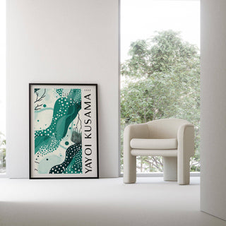Black White and Green Poster with abstract aqua shapes in a black frame leaning next to a beige armchair