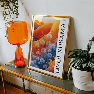 Framed print of abstract floral shapes in blue and orange leaning on a table with an orange lamp