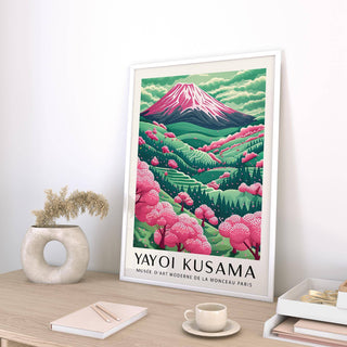 Framed Mountain Landscape print with pink cherry blossoms leaning on a wooden desk with a neutral vase