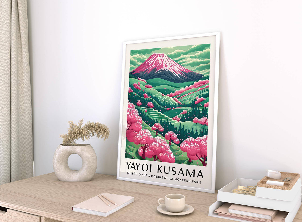 Framed Mountain Landscape print with pink cherry blossoms leaning on a wooden desk with a neutral vase