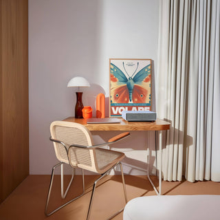 Print leaning on desk of butterfly wall art with blue and orange wings and table lamp