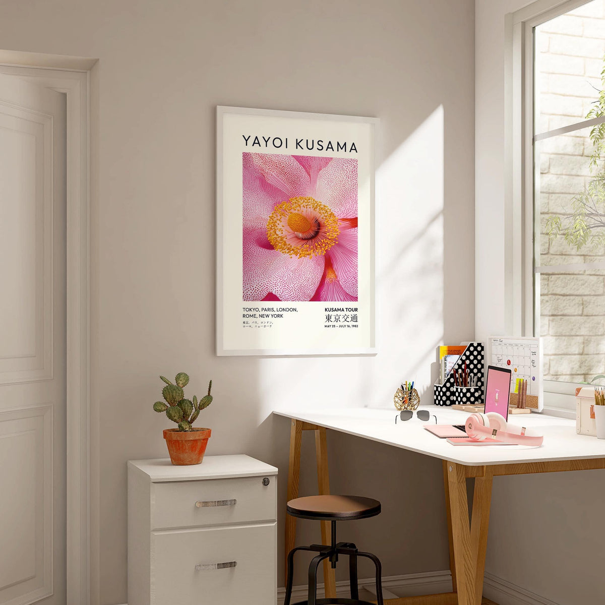 Abstract Pink wall art of a pink blossom flower with orange stamens hung above a desk with a small cactus