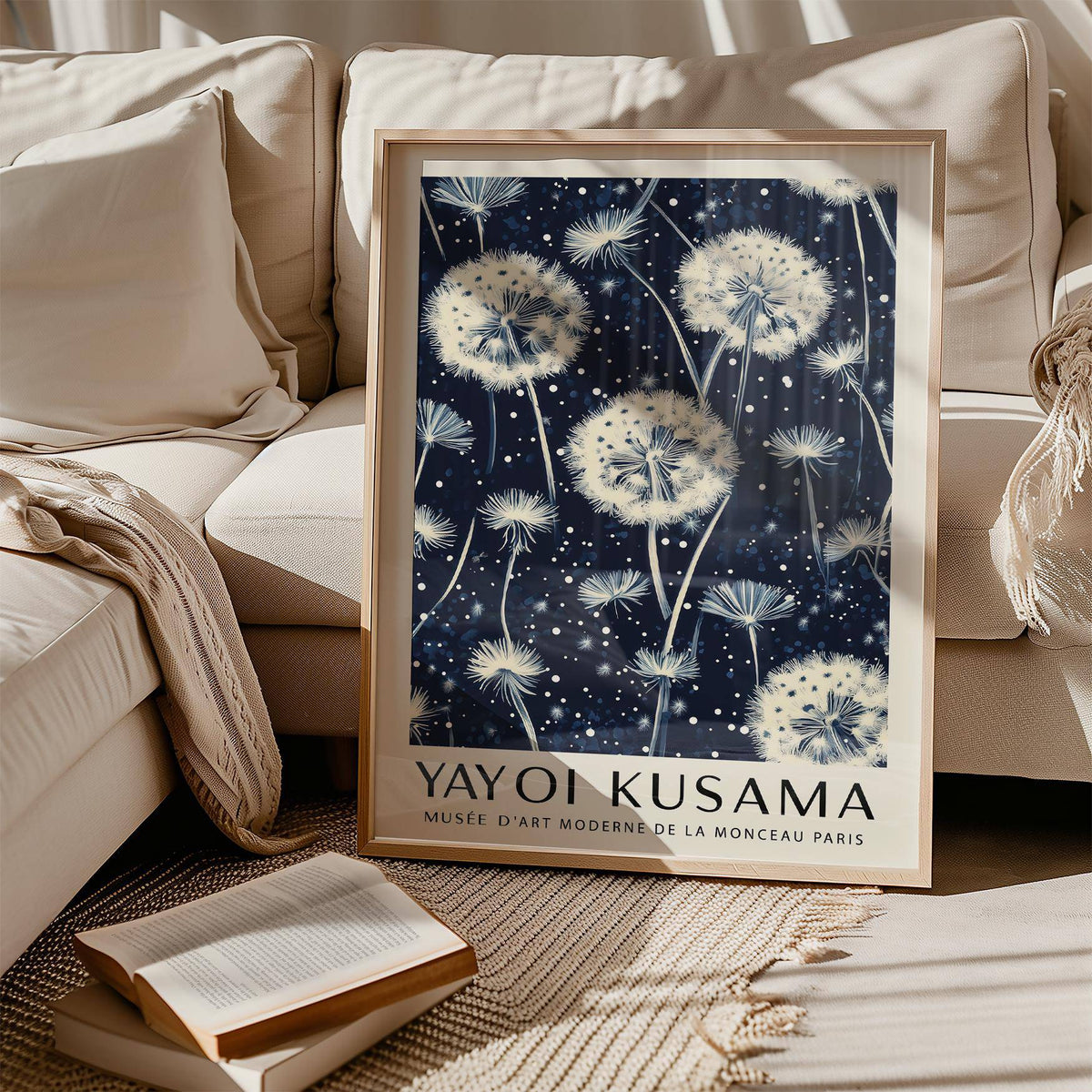 Living room print leaning on sofa of white dandelion seed heads on dark blue background with text below