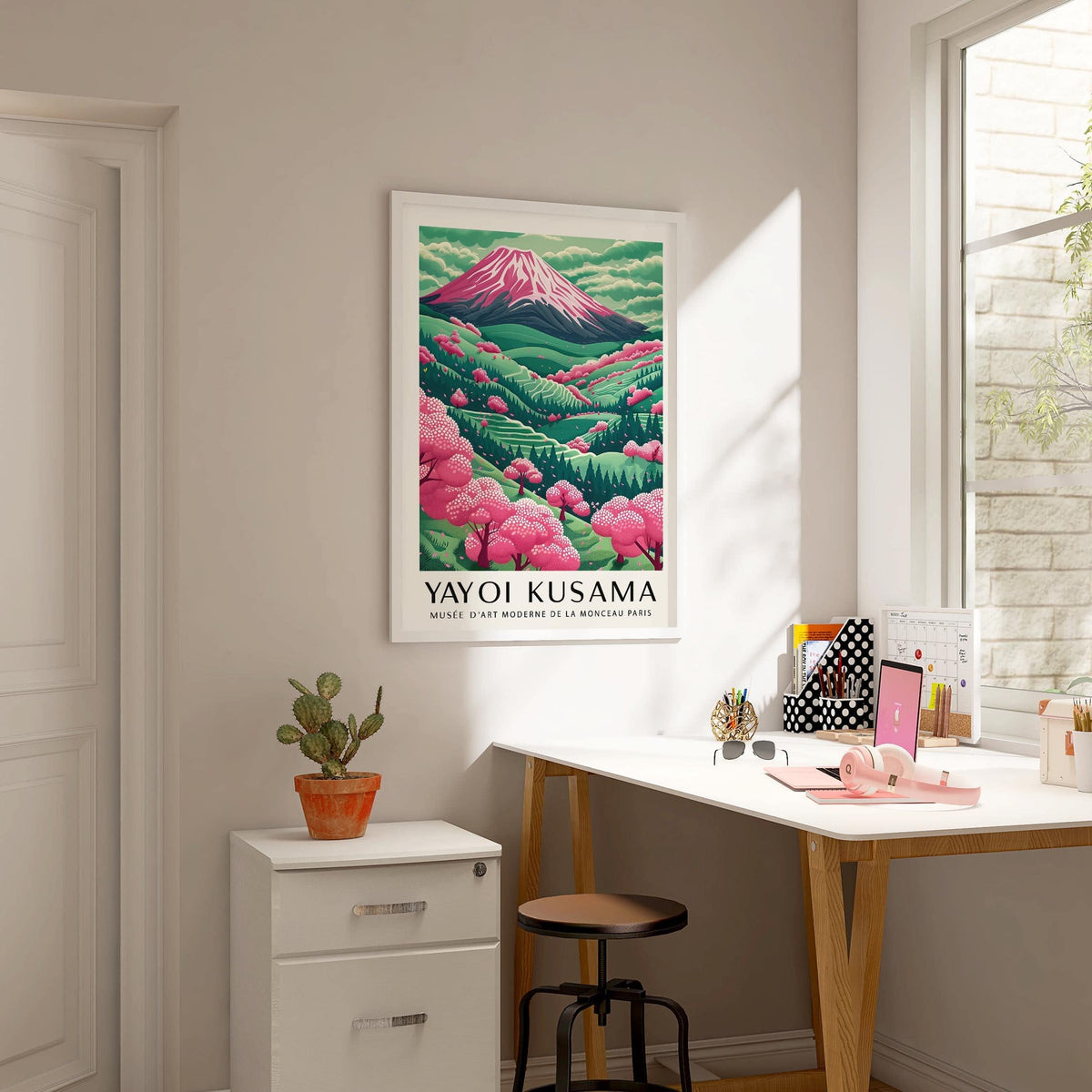 Mountain Landscape wall art with pink cherry blossom trees and green hills hanging above a cabinet with a cactus