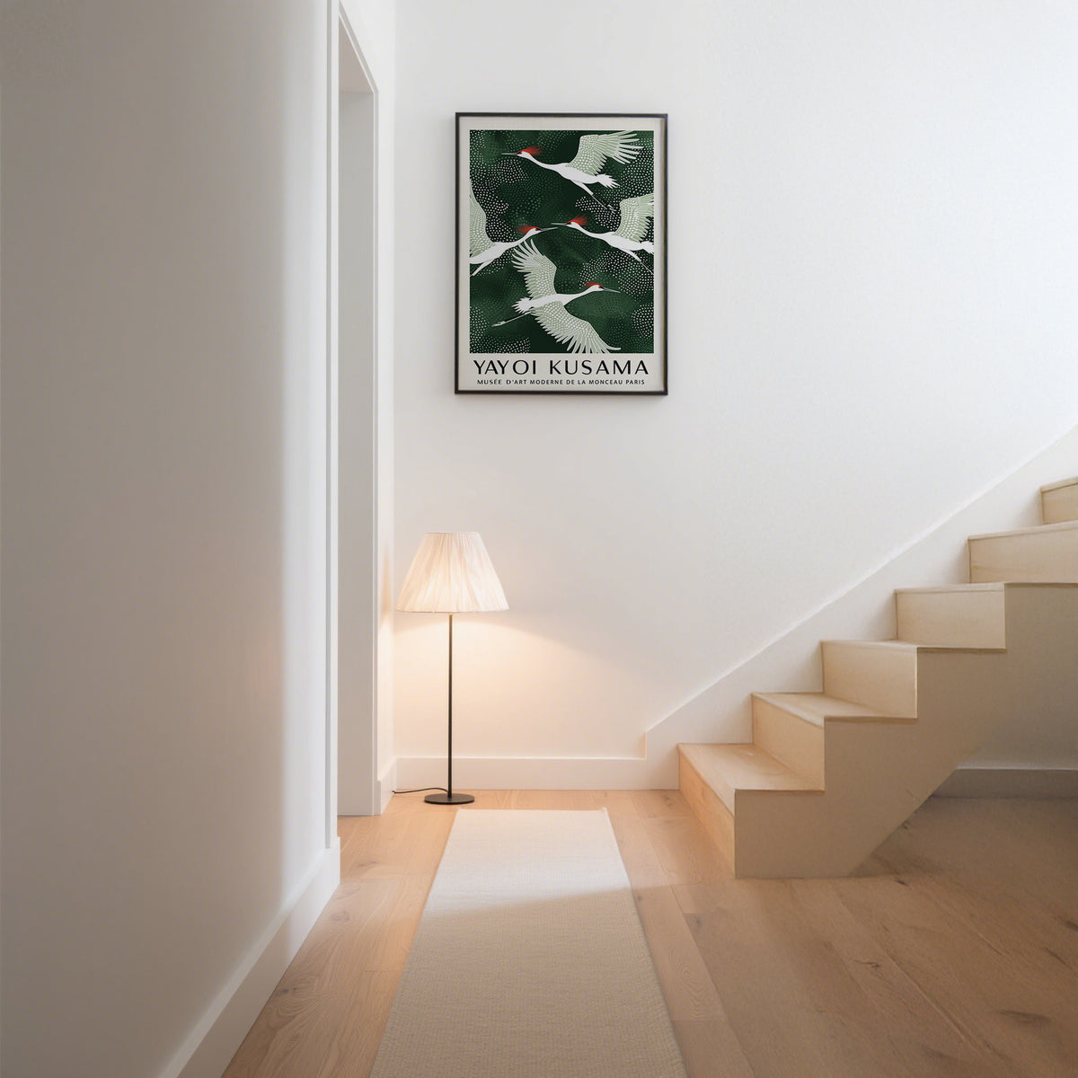 Japandi wall art of red-crowned cranes flying in white and green hung above a standing lamp in a corridor