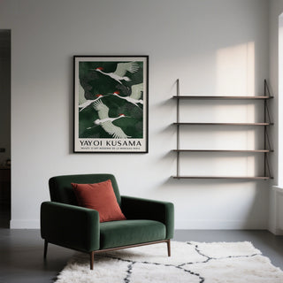 Japandi wall art with white and red cranes flying against a dark green background above a green armchair with a red cushion