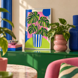 Striped Pot Monstera Print, a small A4 framed print leaning on a colourful lacquered shelf in a living room