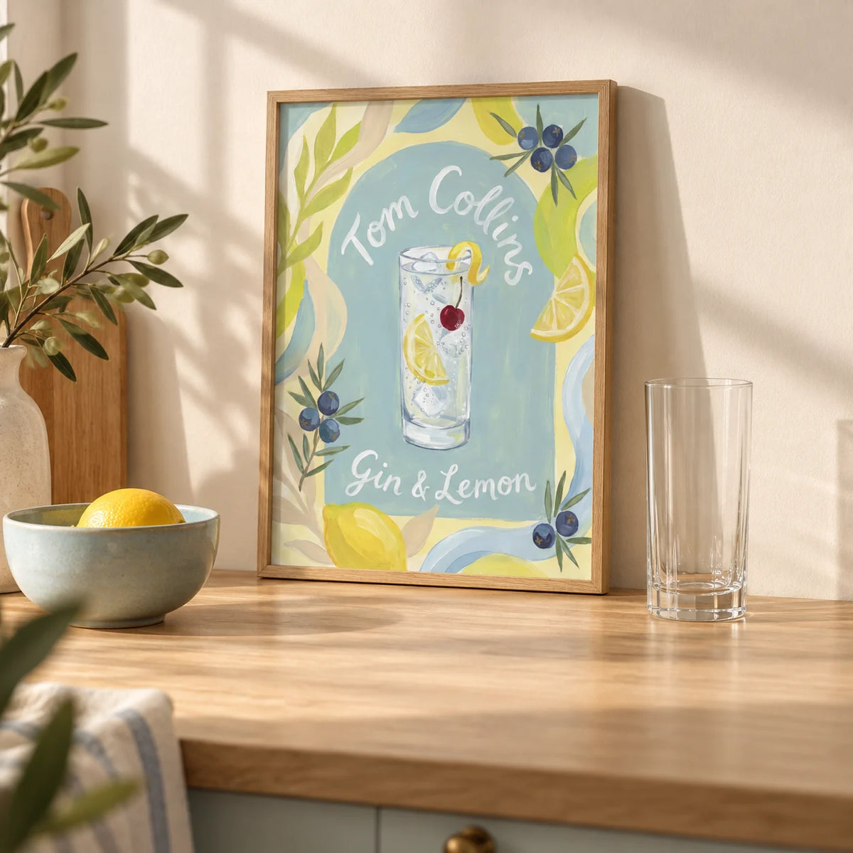 Tom Collins Art Print, a small A4 framed print leaning on a pale oak kitchen worktop
