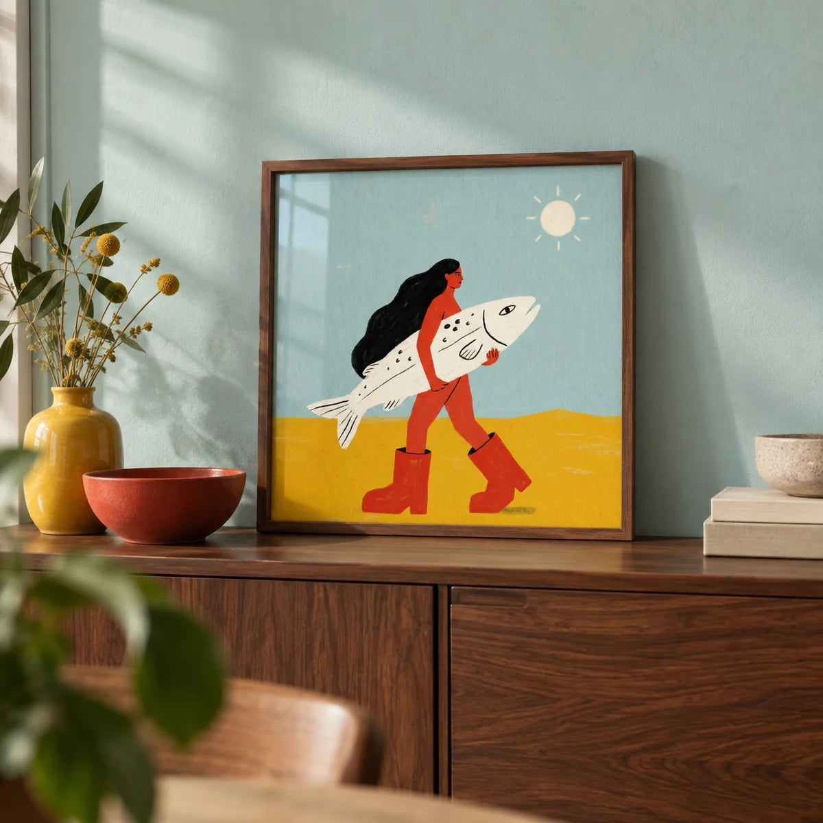 Woman Carrying Fish Print, a small A4 framed print leaning on a walnut sideboard in a living room