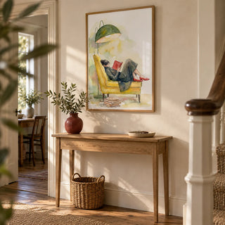 Woman Reading In Armchair Print, framed on the wall of a welcoming hallway in a compact UK period home with pale stone walls and wooden floorboards