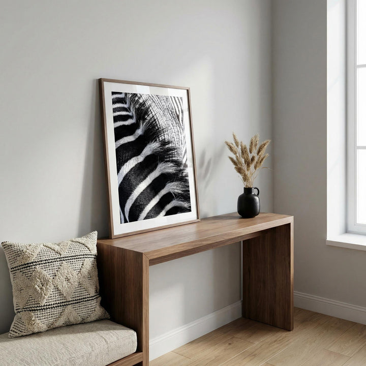 Framed Zebra Stripe Art Print with black and white striped close-up leaning on a wooden table with a black vase beside it